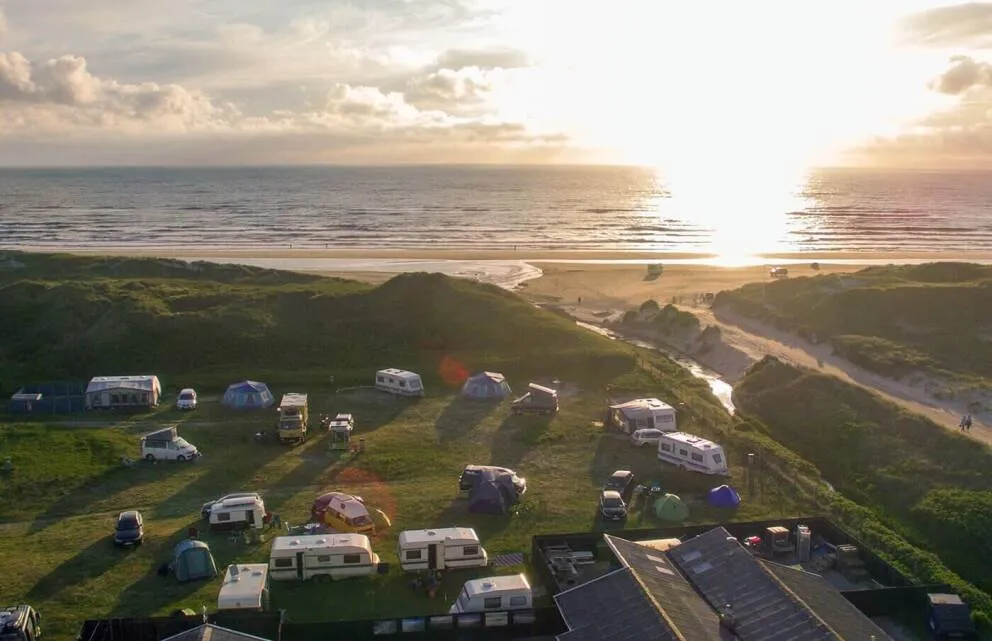 Aerial view of Børsmose Strand Camping: caravans and tents in the dunes above a wide North Sea beach at sunset