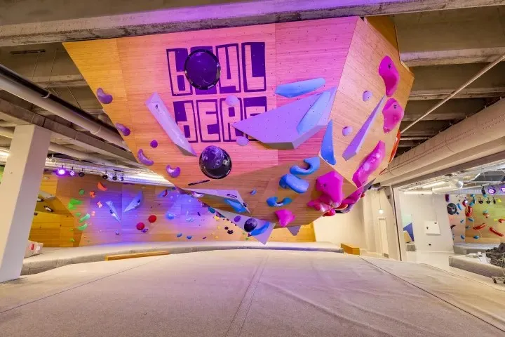 The Boulders DK climbing hall: a tilted wooden wall studded with coloured holds under purple light