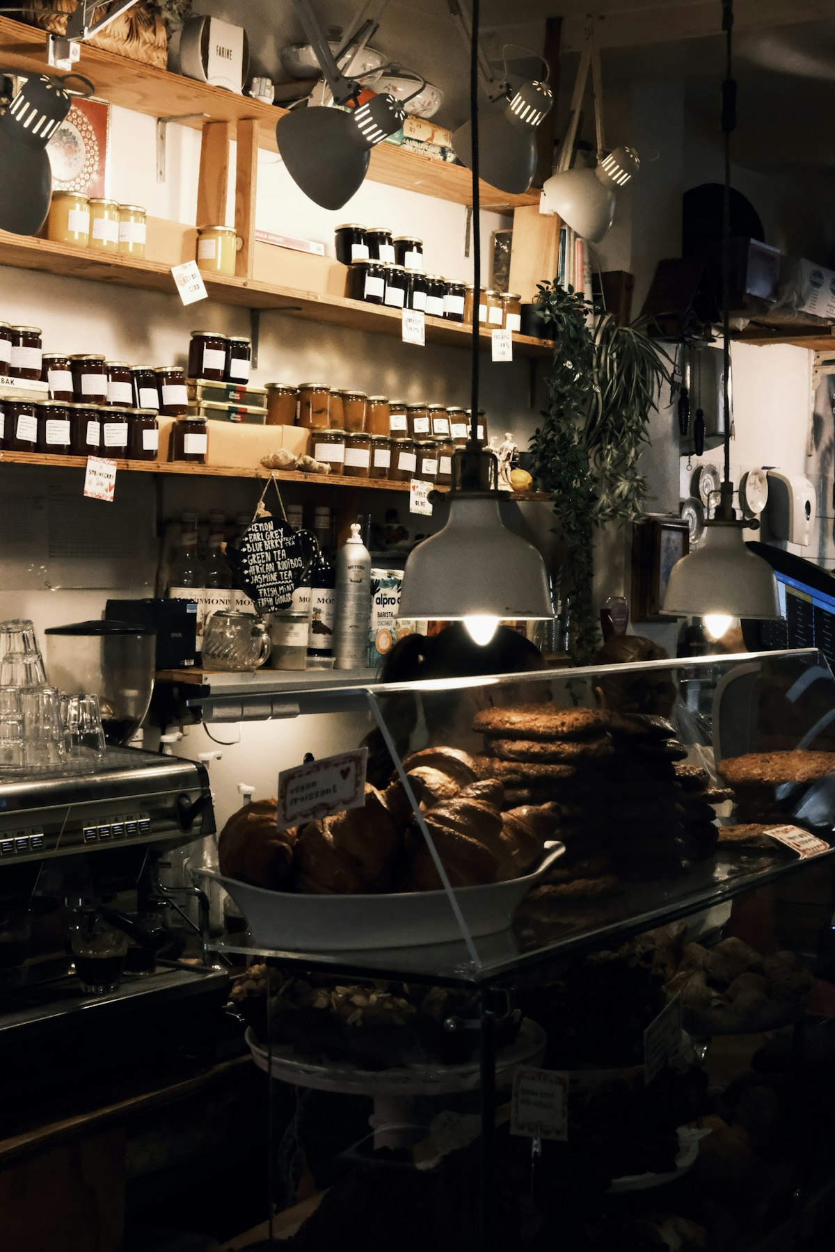 A warmly lit bakery counter with pastries under glass and shelves of preserves behind